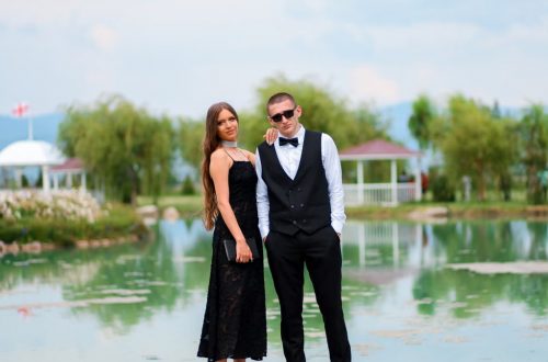 A couple in formal attire poses elegantly by a serene lake, capturing a romantic moment.