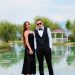 A couple in formal attire poses elegantly by a serene lake, capturing a romantic moment.